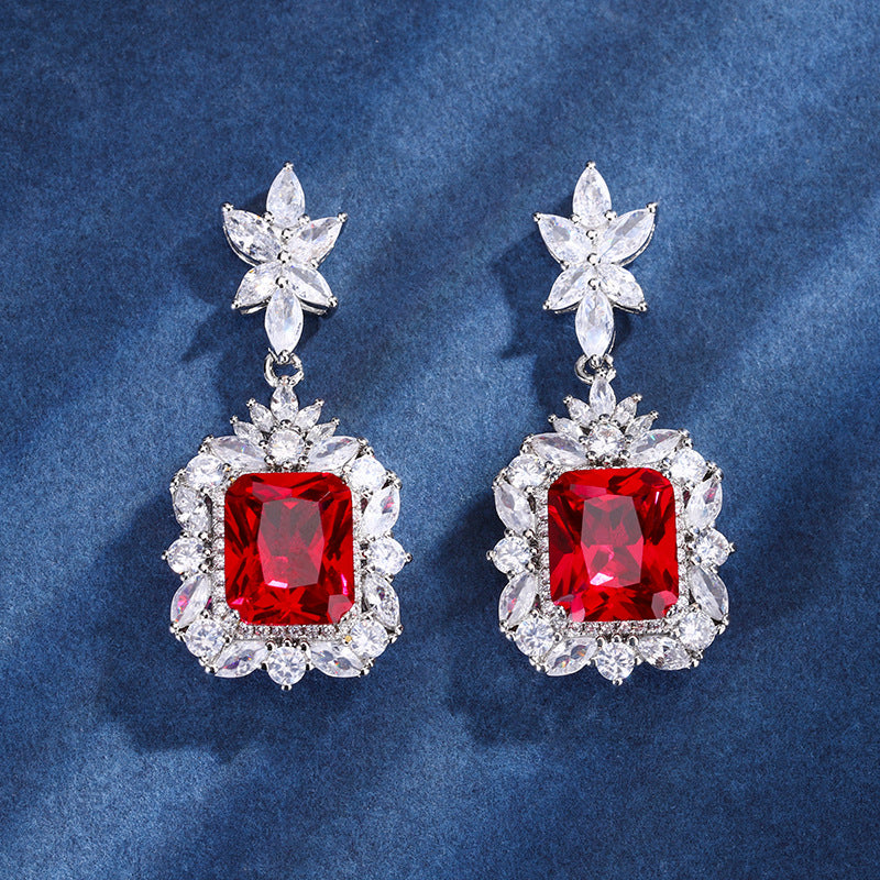 Pair of earrings with red gemstones and star-shaped tops on a blue background