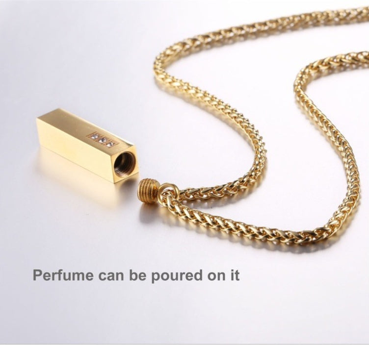Gold necklace with a cylindrical gold pendant on a light gray background