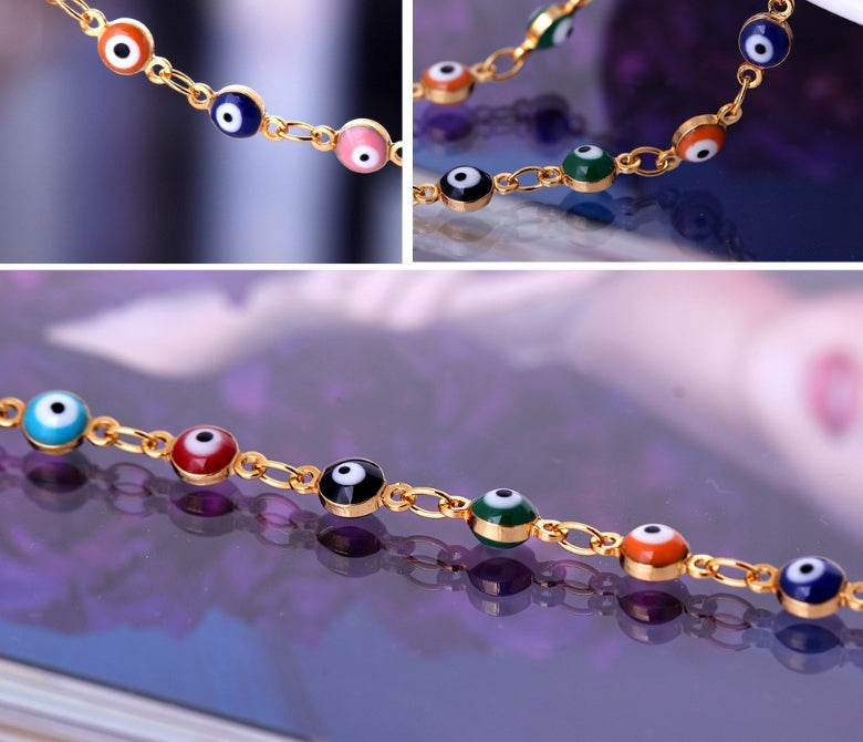 Gold bracelet with colorful eye-shaped beads on a reflective surface