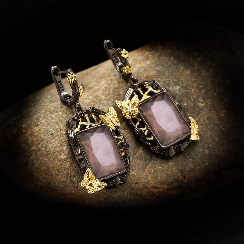 Pair of ornate earrings with purple stones on a textured surface