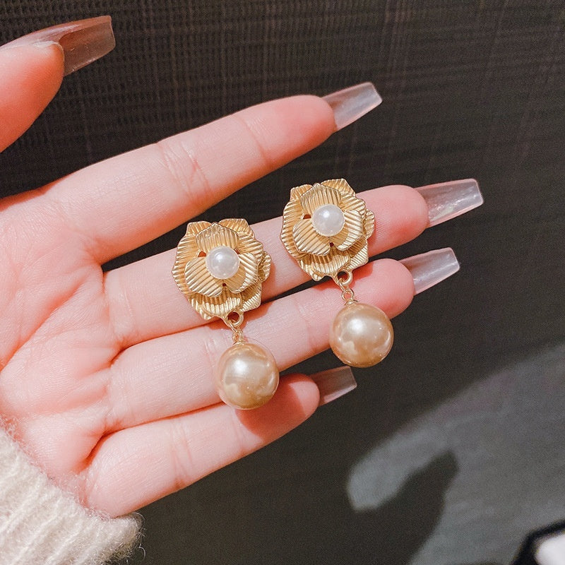 Gold earrings with pearl drops held in a hand against a dark background