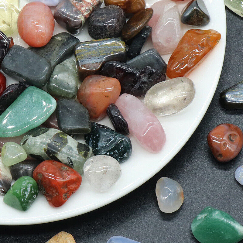 Assorted colorful gemstones on a white plate with additional stones on a black surface.