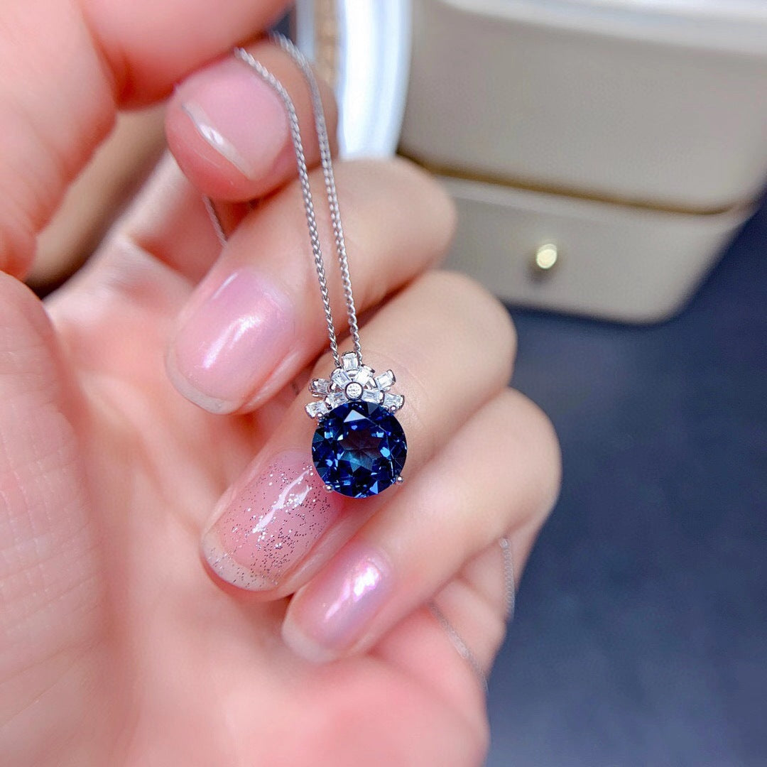 Hand holding a necklace with a blue gemstone pendant against a blurred background