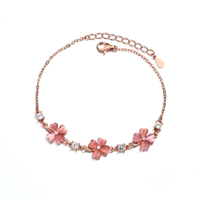 Rose gold bracelet with pink floral charms on a white background