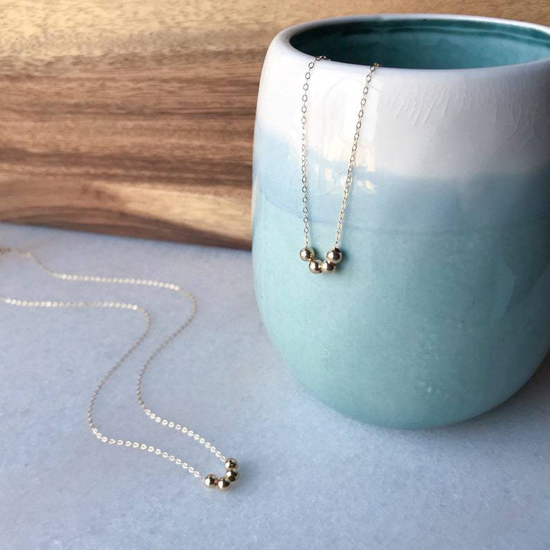 Necklace with small beads draped over a light blue ceramic pot on a wooden surface.