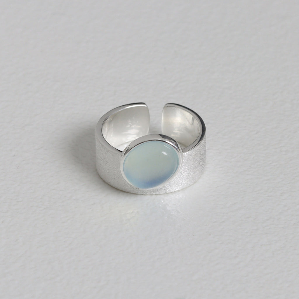 Silver ring with a round, light blue stone on a gray background