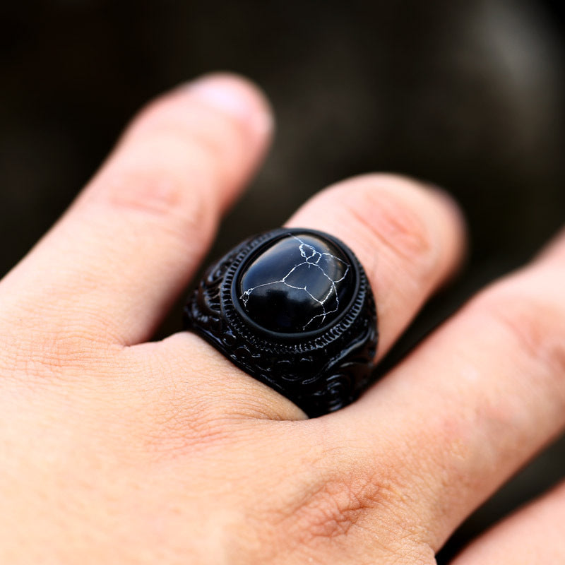 Black ring with a detailed design worn on a finger against a dark background