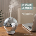 Silver disco ball humidifier on a desk with a laptop, emitting mist.