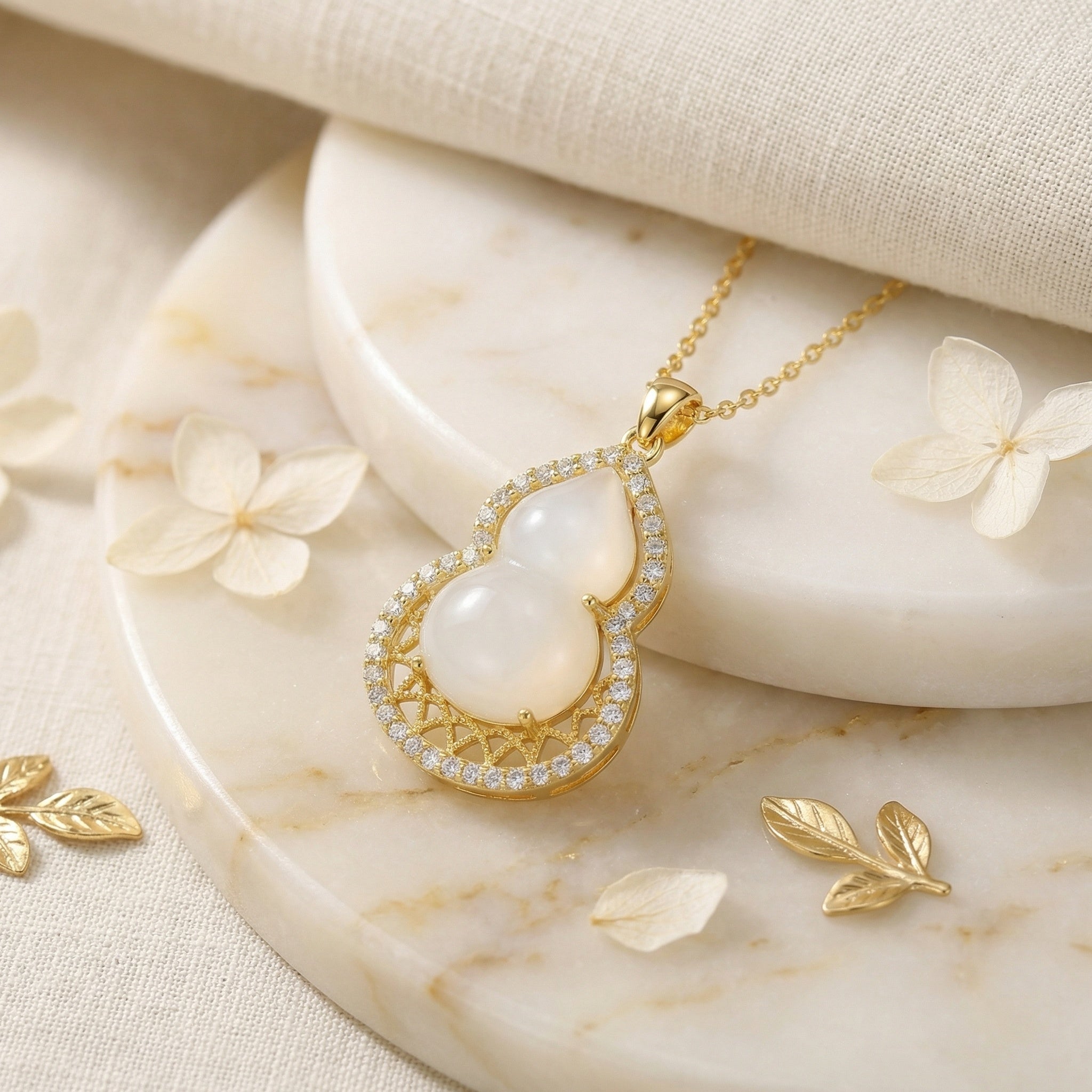 Gold necklace with a white pendant on a marble surface with flowers
