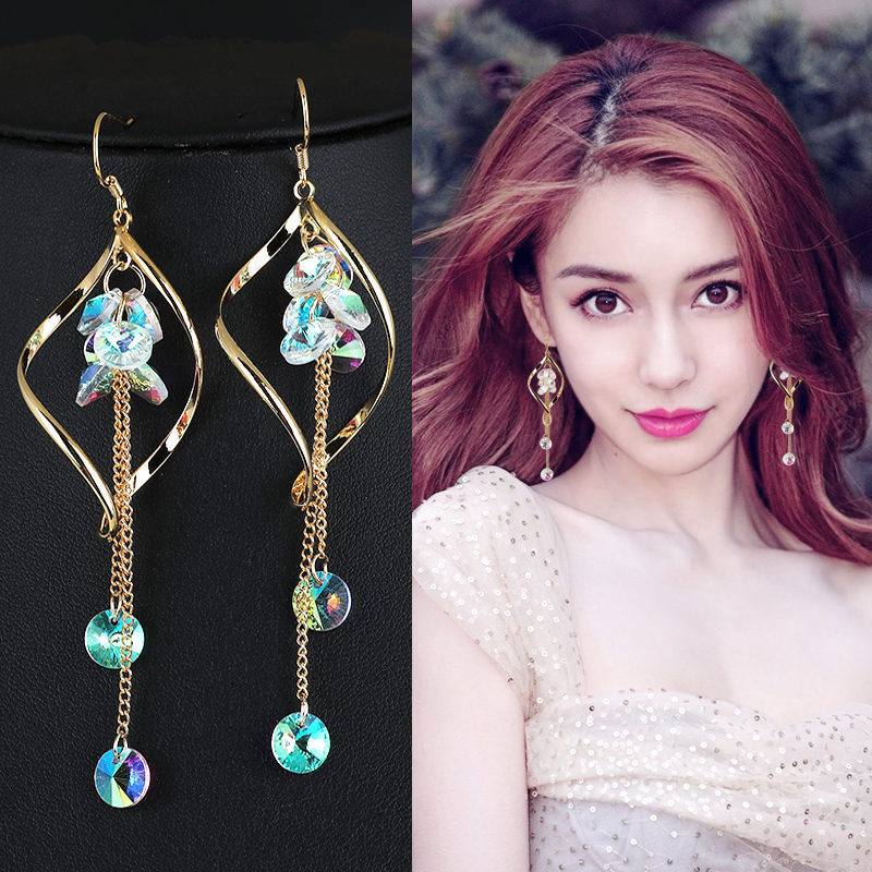 Gold earrings with colorful stones on a black background, worn by a model.