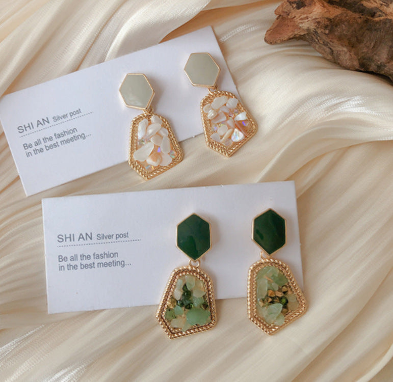 Two pairs of earrings on white cards with 'SHI AN' branding, placed on a textured beige surface.