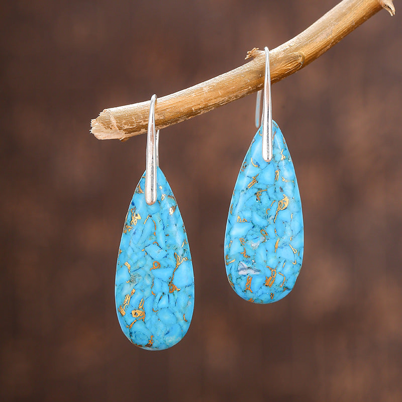 Turquoise teardrop earrings with gold specks hanging on a branch against a brown background