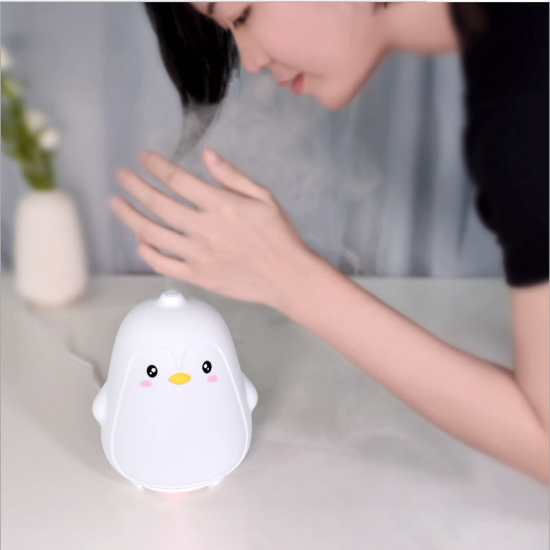 Person interacting with a cute penguin-shaped night light on a table.
