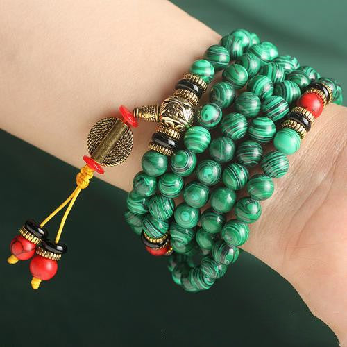 Green beaded bracelet with red and gold accents on a wrist against a dark background