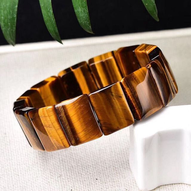 Brown beaded bracelet on a white surface with green leaves in the background