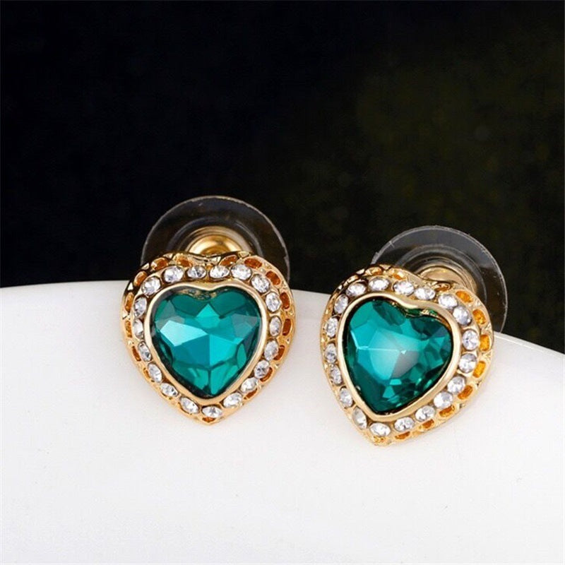Heart-shaped earrings with teal gemstones and gold accents on a white surface.