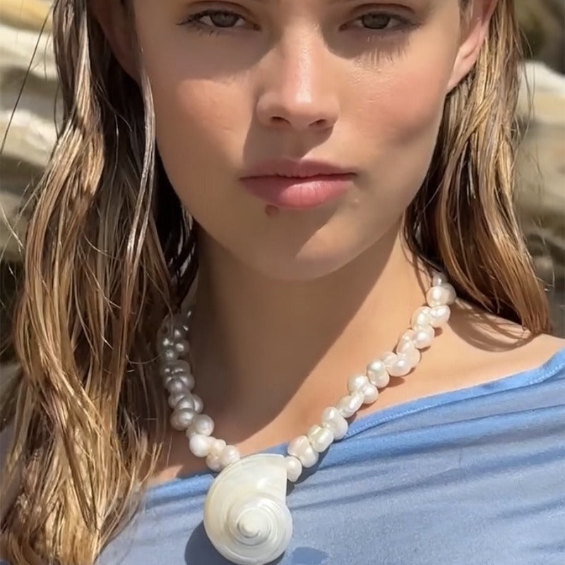 Woman wearing a pearl necklace with a shell pendant outdoors