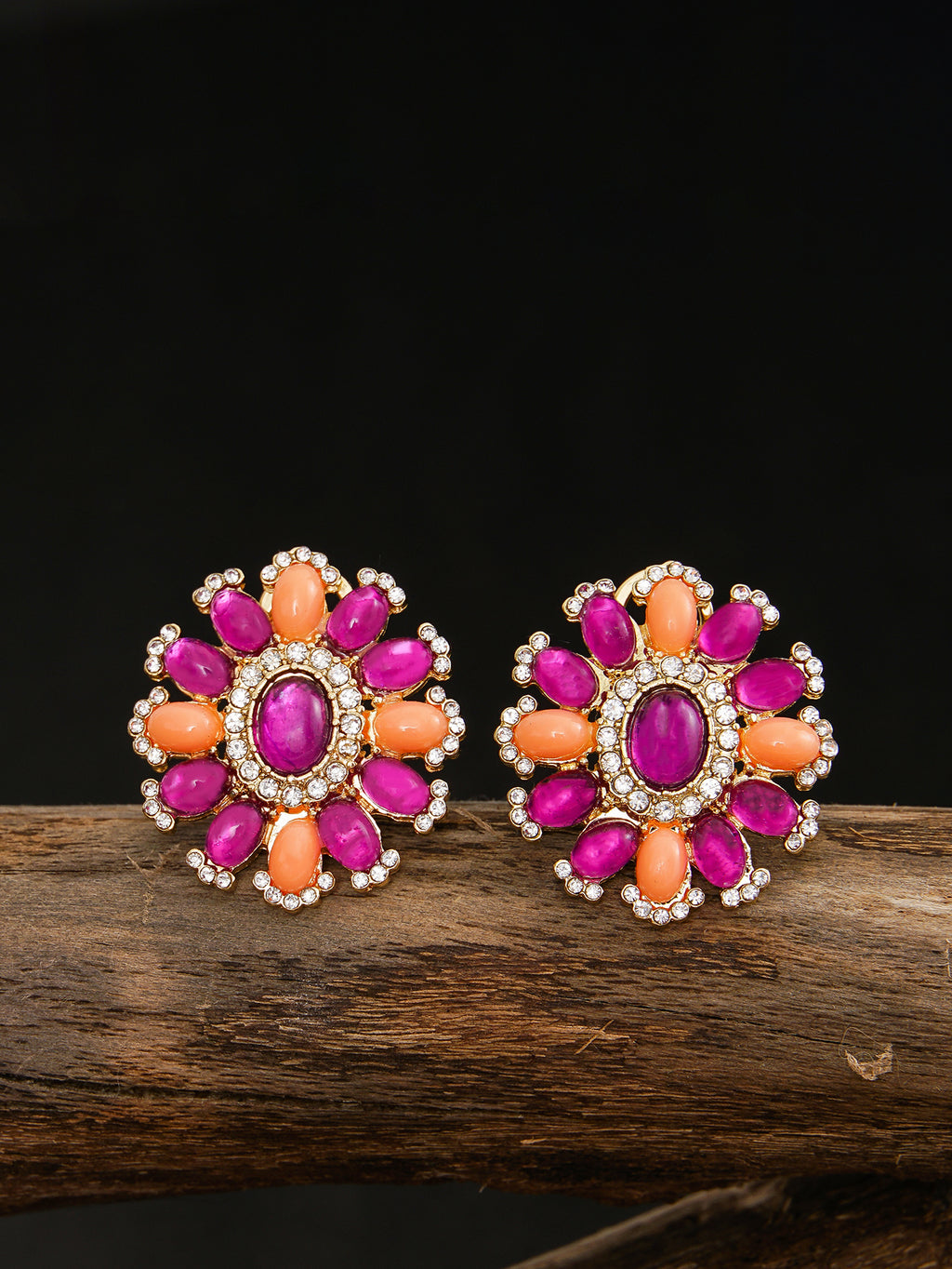 Pair of floral earrings with pink and orange stones on a wooden surface.