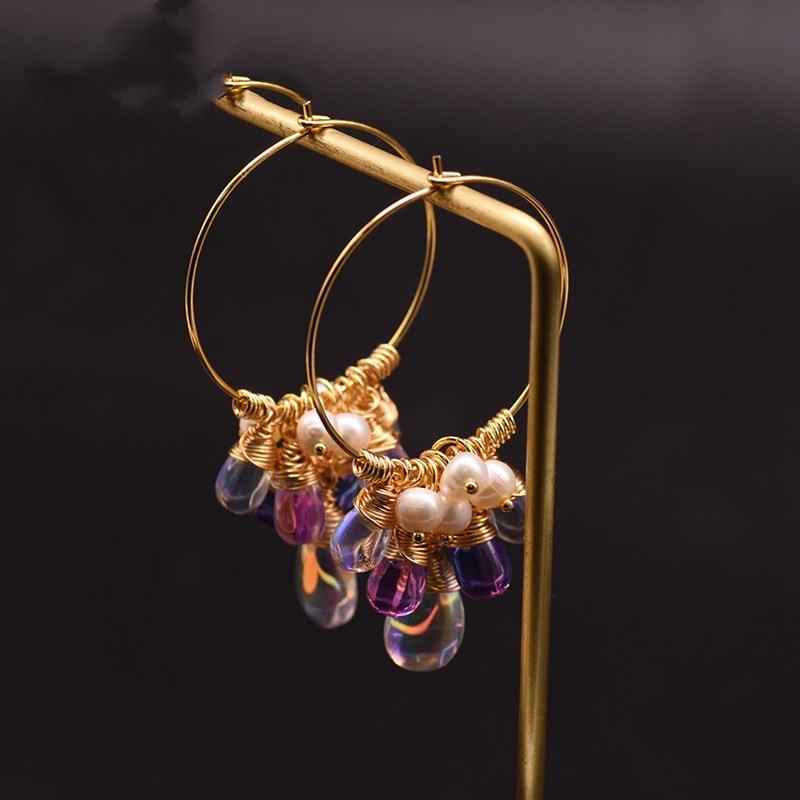 Gold hoop earrings with pearls and purple beads on a dark background