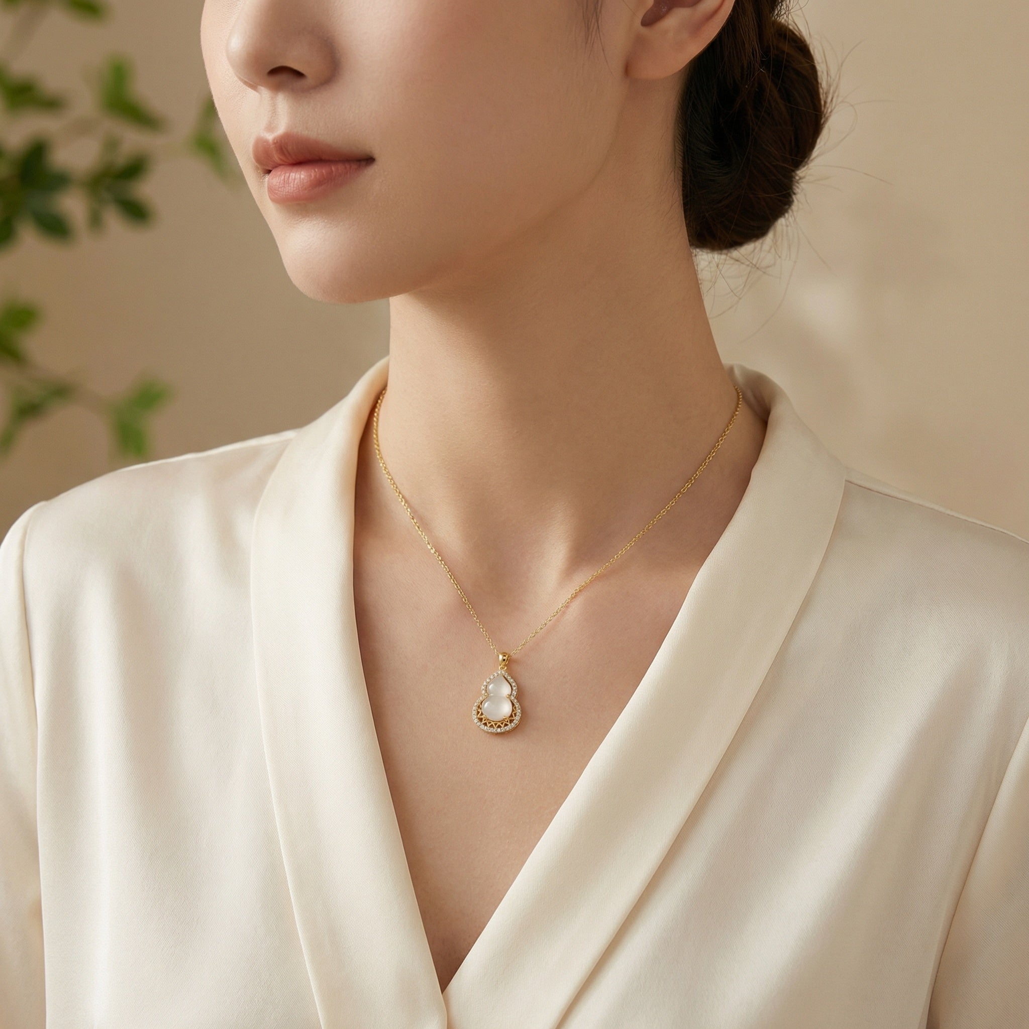Woman wearing a gold necklace with a pearl pendant against a neutral background