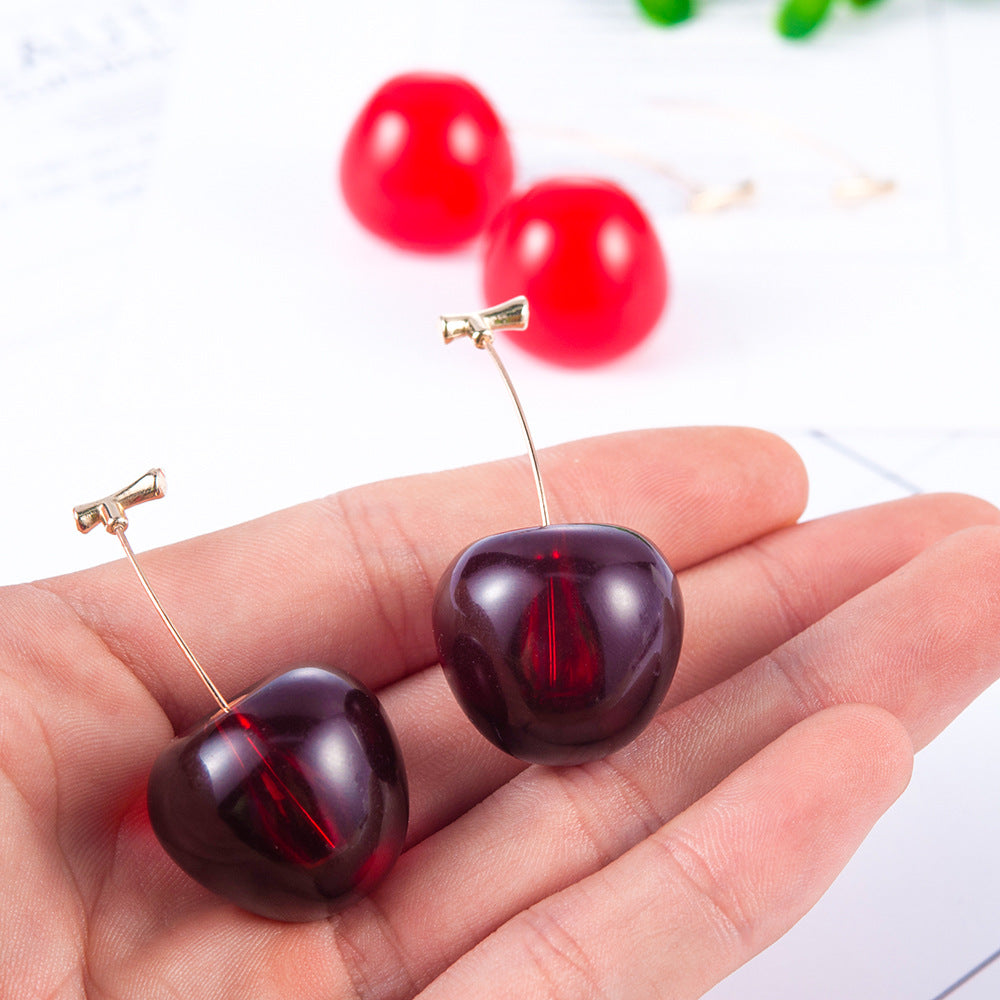 Red cherry-shaped earrings held in a hand with a blurred background