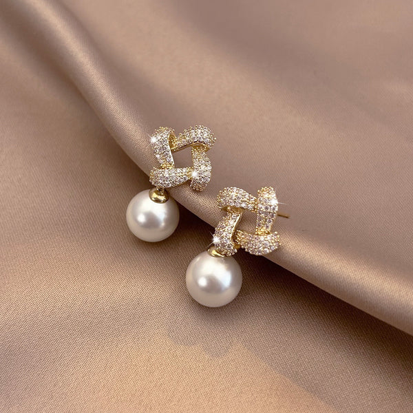 Pair of pearl earrings with gold and diamond accents on a beige fabric background