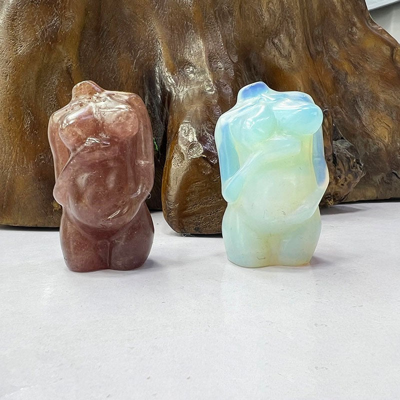 Two stone sculptures of nude figures on a white surface with a wooden background
