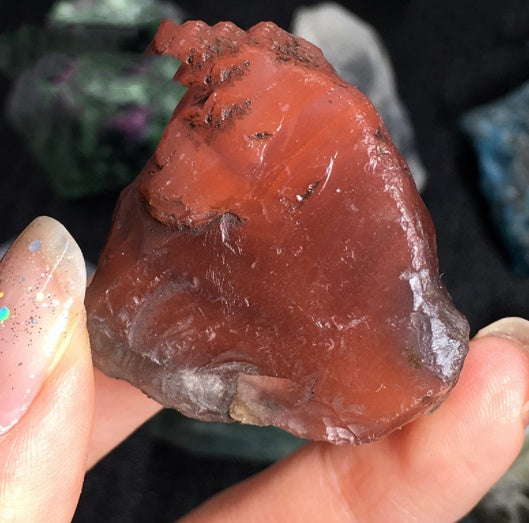 Raw red jasper stone held between fingers with a blurred background