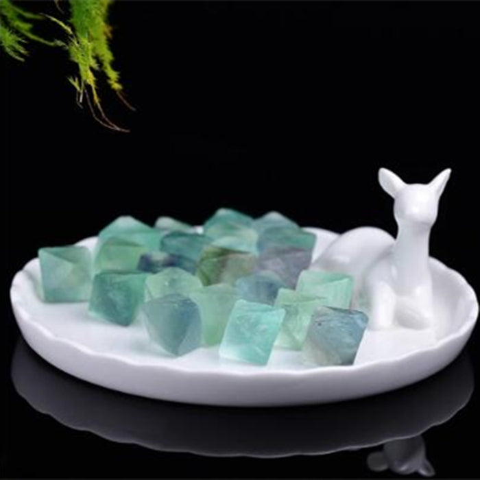 Decorative dish with green crystals and a white deer figurine on a black background