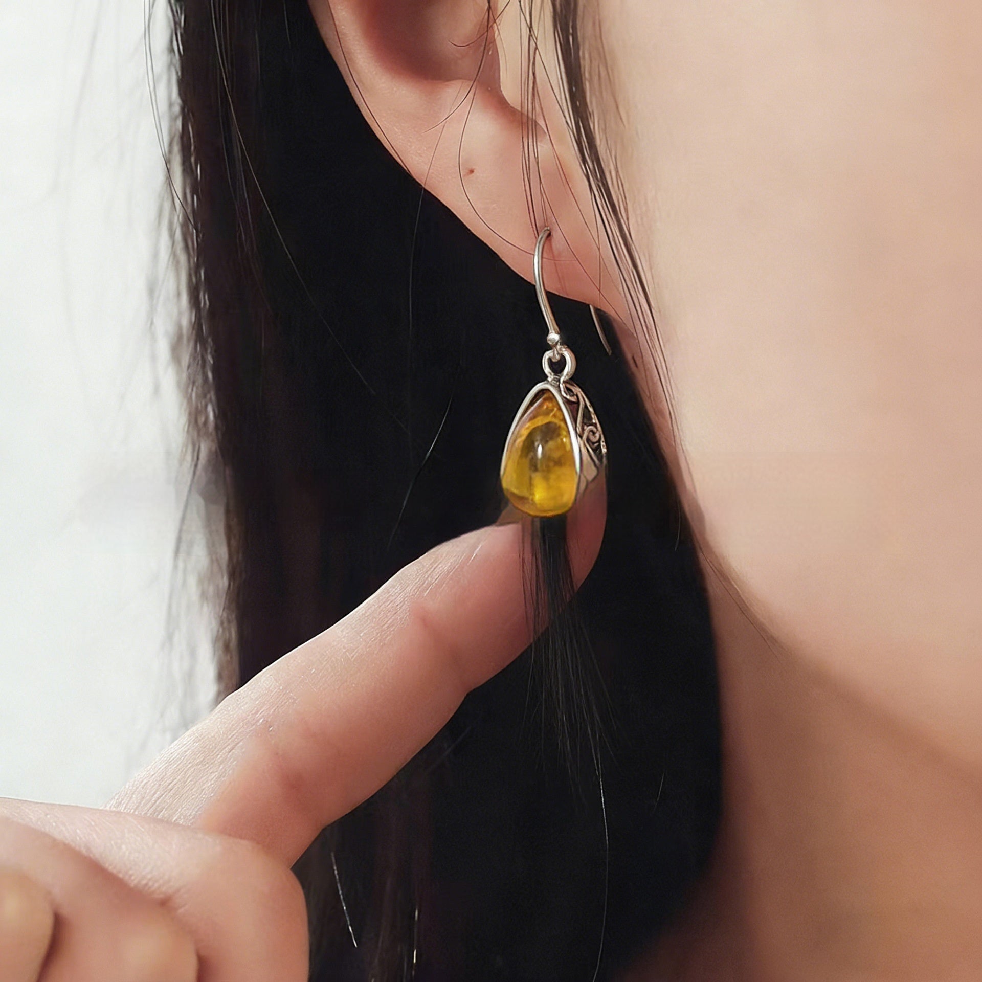 Close-up of a person wearing an amber teardrop earring with a silver setting.