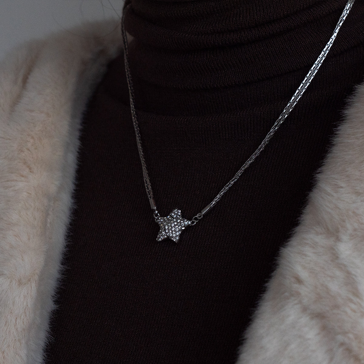 Star-shaped necklace on a black turtleneck against a fur background