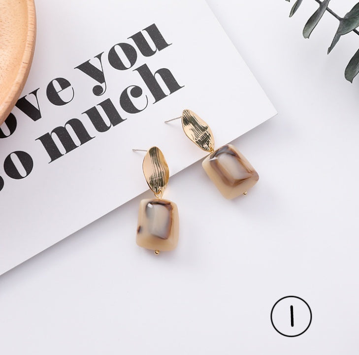 Pair of gold and brown earrings on a white surface with a piece of paper underneath.