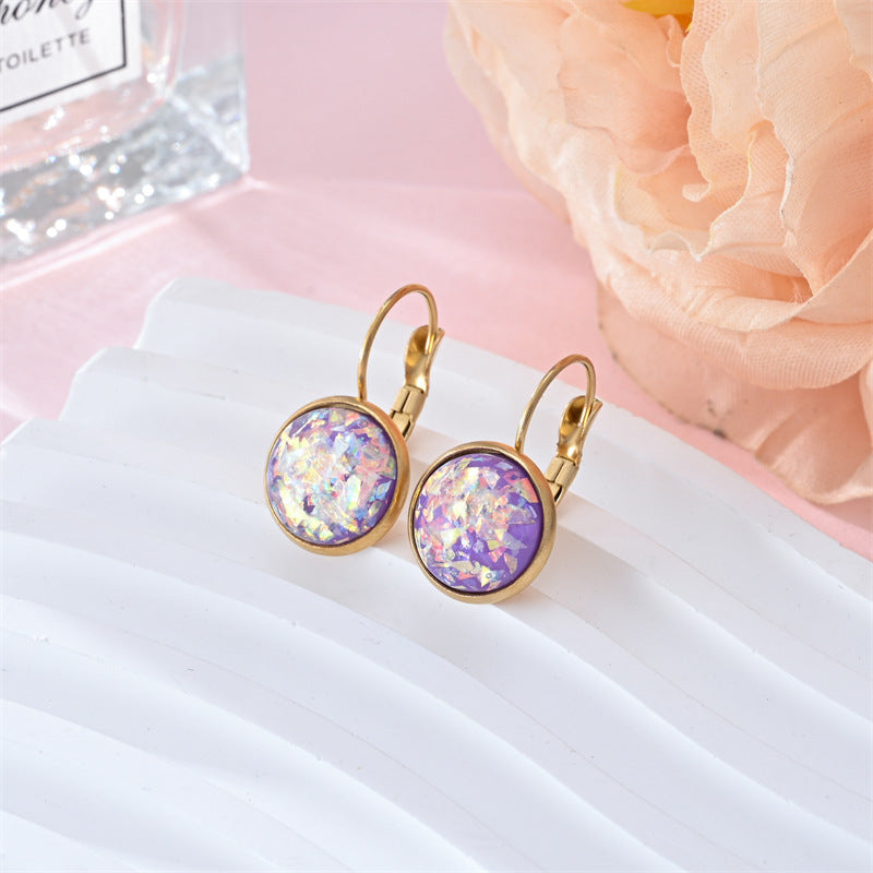 Gold earrings with purple and pink gemstones on a white surface with a pink flower in the background.