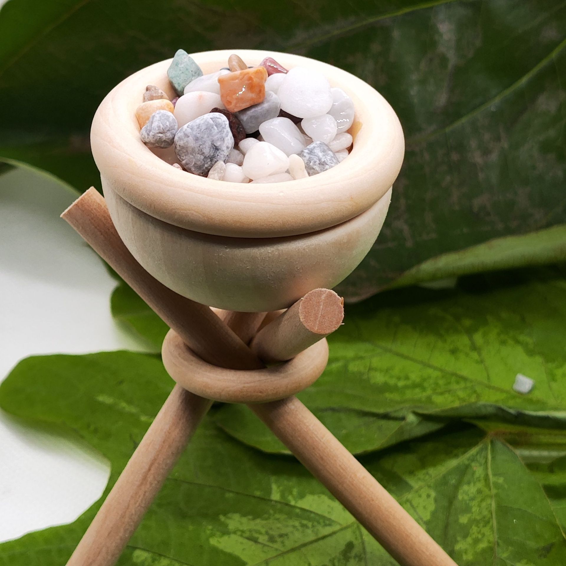 Small wooden bowl with pebbles on a green leaf background