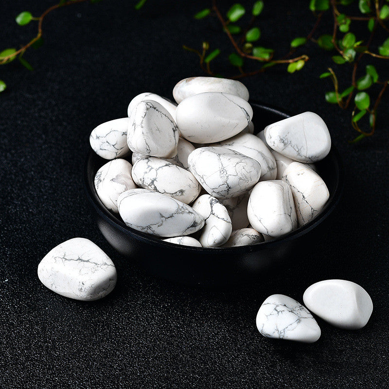 White marbled stones in a black bowl on a dark surface with greenery.