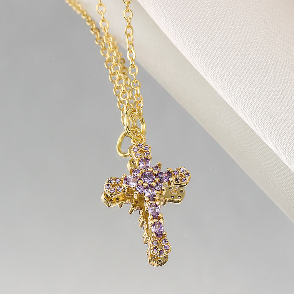 Gold necklace with a cross pendant featuring purple stones on a light gray background