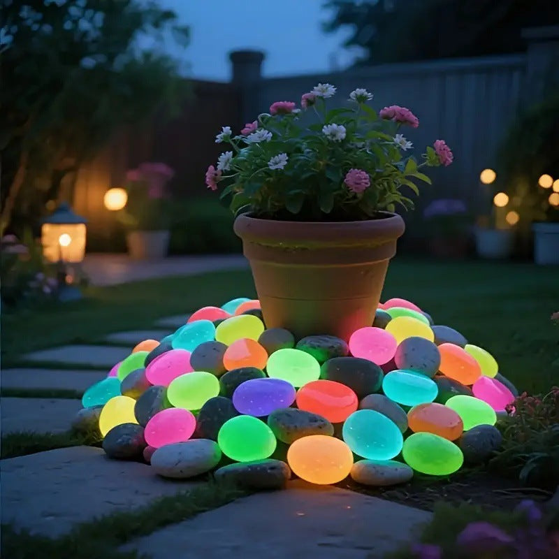 Glowing multicolored stones arranged around a potted plant in a garden setting at night.