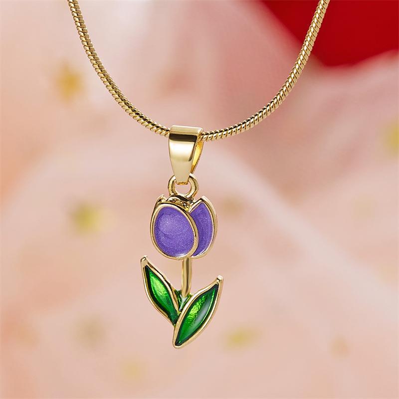 Gold necklace with a purple and green pendant on a soft pink background