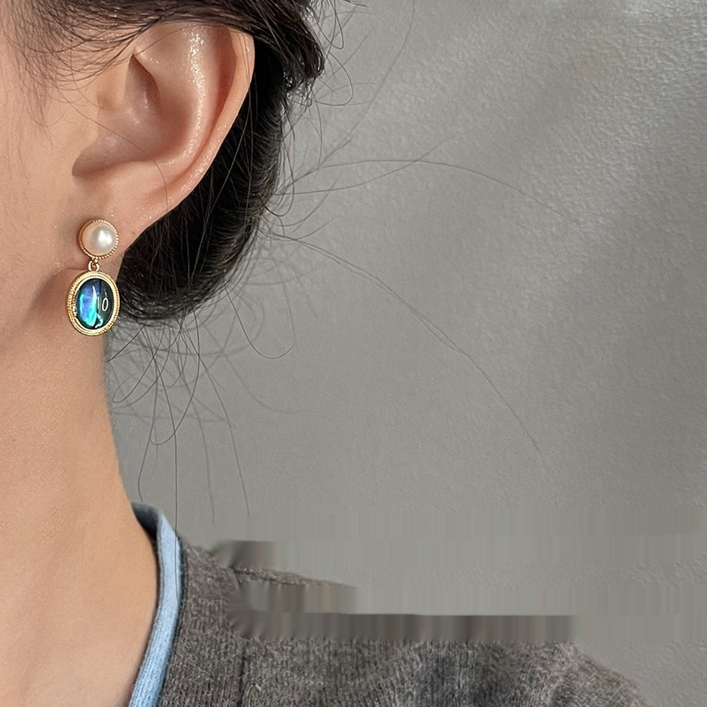 Close-up of an earring with a gemstone and pearl on a neutral background
