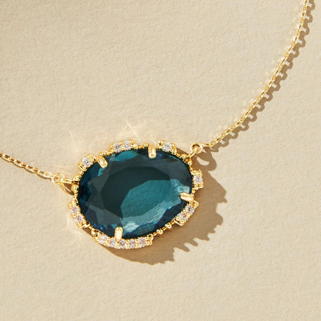 Gold necklace with a large blue gemstone on a beige background