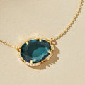 Gold necklace with a large blue gemstone on a beige background