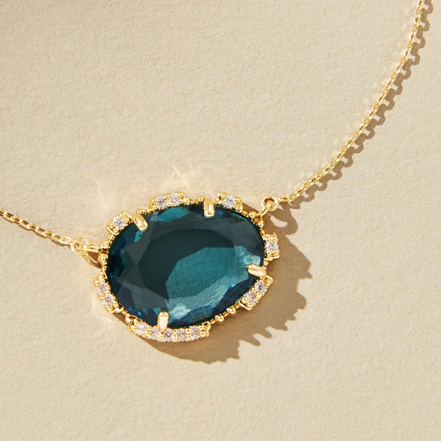 Gold necklace with a large blue gemstone on a beige background