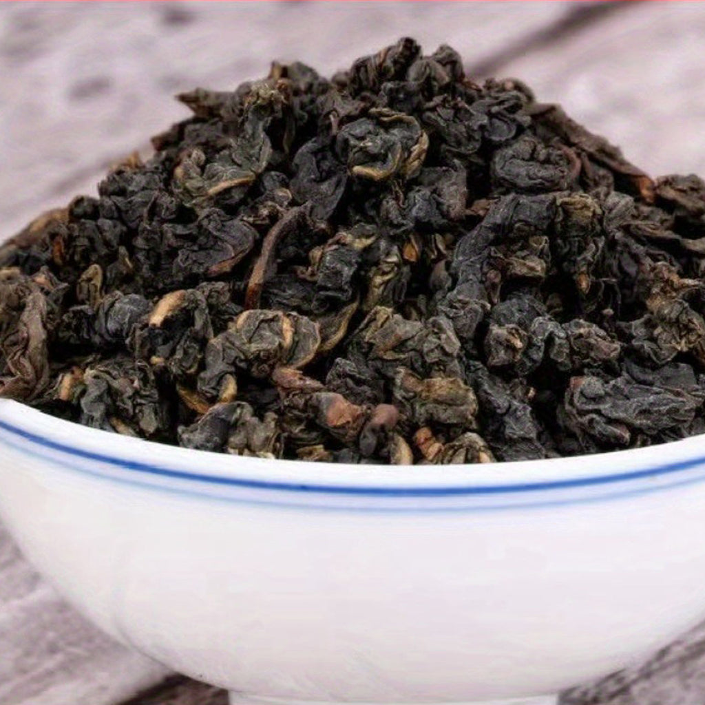 Dry black tea leaves in a white bowl with blue rim on a wooden surface