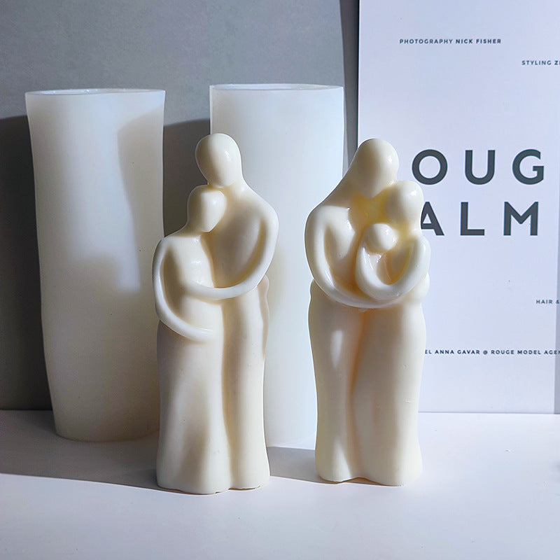 Two white ceramic figures of a family holding a child, with a large white candle behind them.