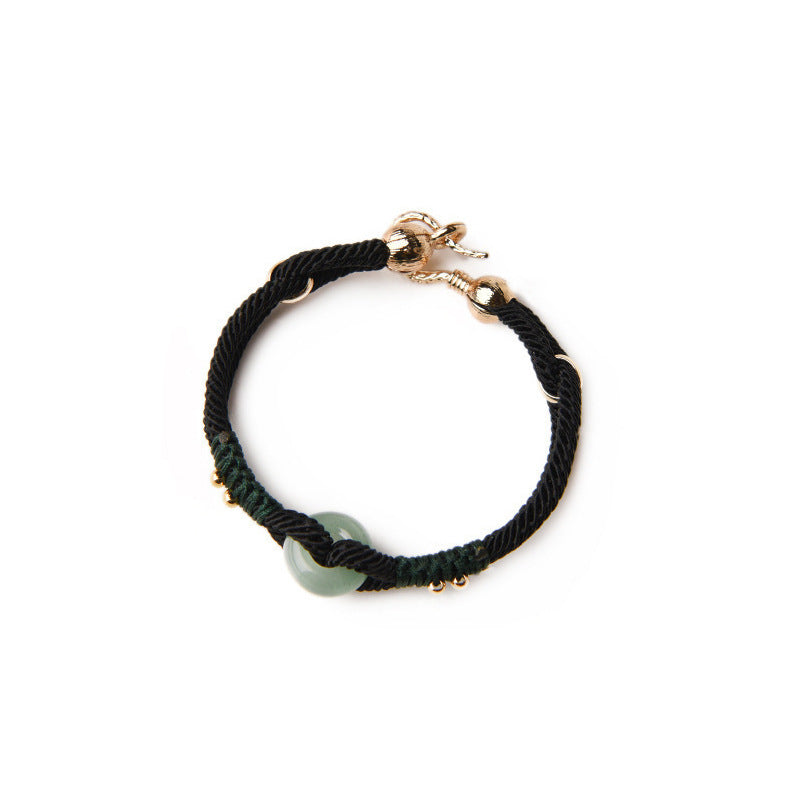 Black braided bracelet with a gold clasp and green bead on a white background
