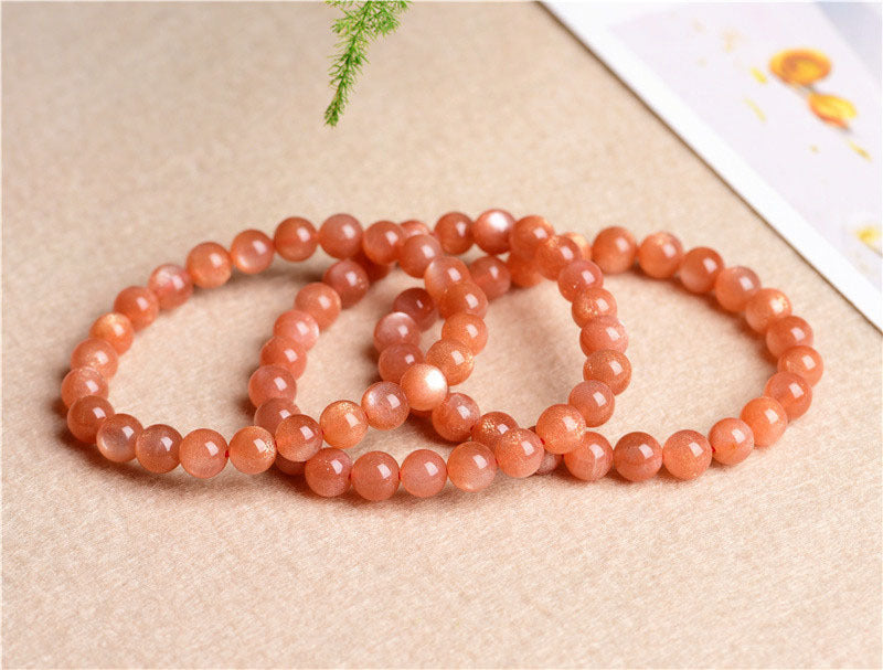 Three peach-colored beaded bracelets on a beige surface with a white card in the background.