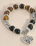 Bracelet with brown and black beads and a silver heart charm on a beige background
