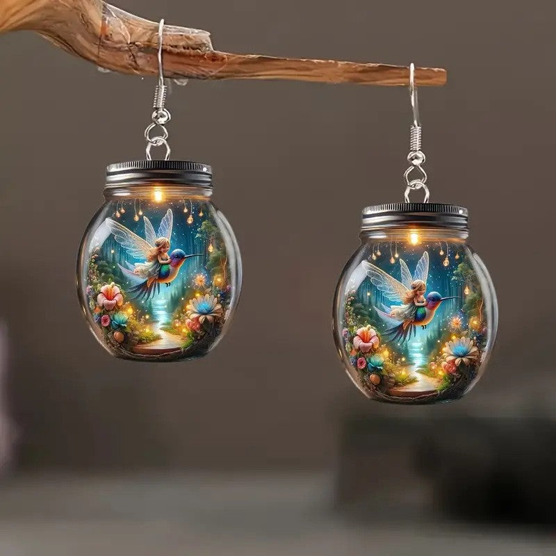 Glass jar earrings with fairy and floral design on a wooden branch against a dark background