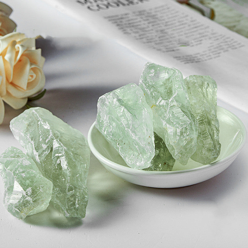 Green crystals in a white bowl on a light surface with a newspaper and flowers in the background.