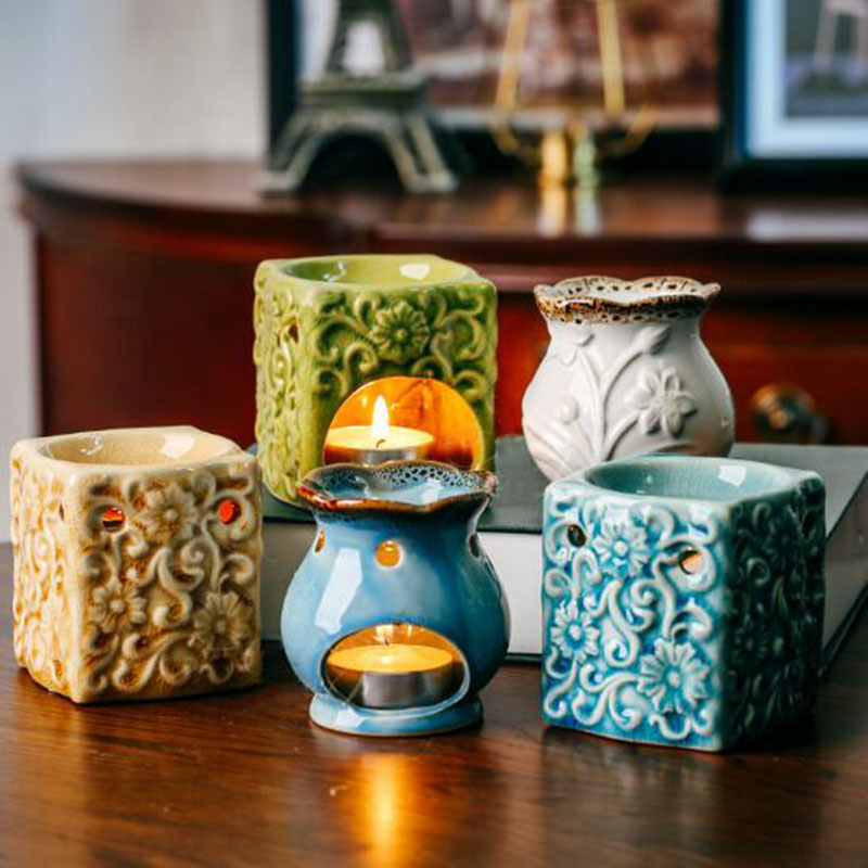 Five ceramic oil burners of different designs and colors on a wooden surface.